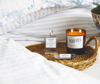 A lifestyle picture of a hand-poured candle, pillow mist, and pulse point oil on white bed linen, promoting deep restful sleep